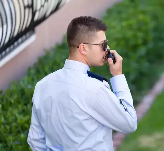 Agent de sécurité à Tiznit en uniforme parlant dans un talkie-walkie, le visage caché pour plus d'intimité, représentant la société de gardiennage locale.t